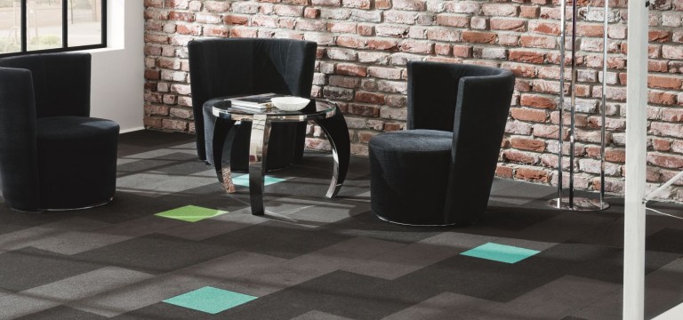 Eine moderne Sitzecke mit drei schwarzen Stühlen um einen Glastisch, auf einem gemusterten Teppich mit grünen und blauen Fliesen von expert Bodenleger, vor einer Sichtziegelwand. -Bodenstyle Schuster - Industriestraße 2 - 66802 Überherrn - +49 (0)6836-7789955