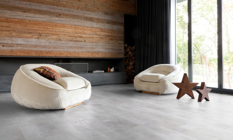 Modernes Wohnzimmer mit zwei großen, weißen, abgerundeten Sesseln, Akzentwand aus Holz, bodentiefen Fenstern und zwei Holzsternen auf hellgrauen Bodenbelägen für einen stilvollen Abschluss. -Bodenstyle Schuster - Industriestraße 2 - 66802 Überherrn - +49 (0)6836-7789955