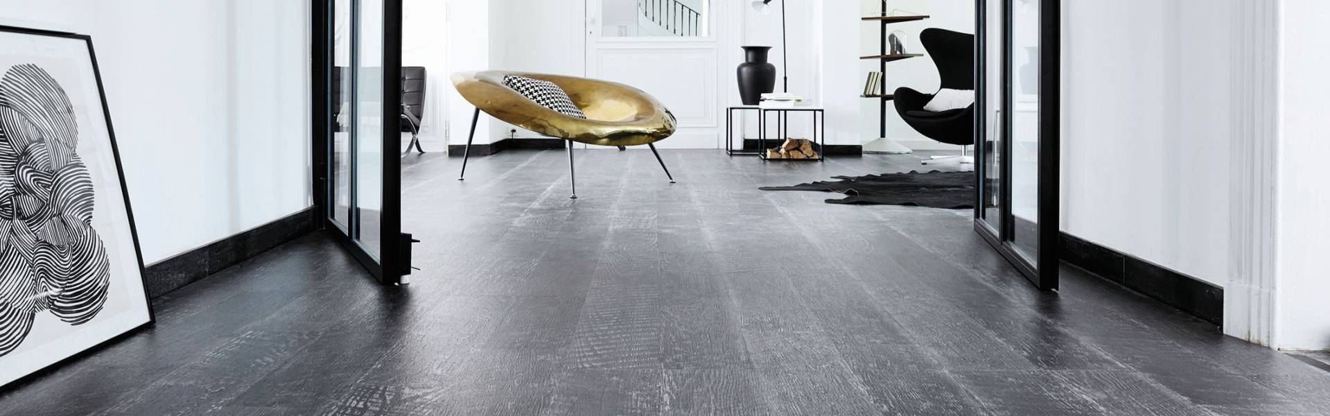Modernes Interieur mit dunklem Holzfußboden, der fachmännisch von einem Bodenleger verlegt wurde, Doppeltüren aus Glas, abstrakte Kunst, ein goldener Akzentsessel, ein schwarzer Sessel und minimalistisches Dekor in einem hellen weißen Raum. -Bodenstyle Schuster - Industriestraße 2 - 66802 Überherrn - +49 (0)6836-7789955