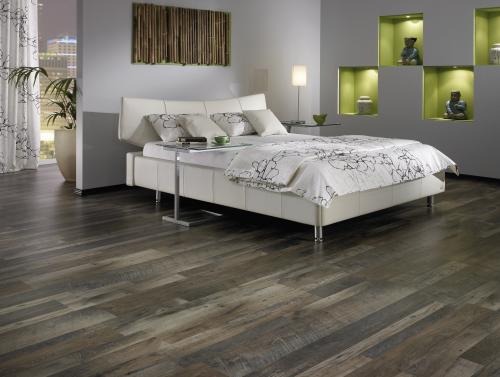 Modernes Schlafzimmer mit weißem Bett, gemusterter Bettwäsche, Laminatbodenbelägen, dunklem Holzfußboden, grün beleuchteten Wandregalen und neutralen Dekorelementen. -Bodenstyle Schuster - Industriestraße 2 - 66802 Überherrn - +49 (0)6836-7789955