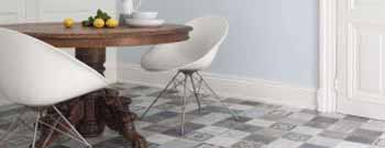 Runder Holztisch mit zwei weißen modernen Stühlen auf gemusterten Bodenbelägen, mit Zitronen und einer Schale auf dem Tisch, vor einer hellblauen Wand. -Bodenstyle Schuster - Industriestraße 2 - 66802 Überherrn - +49 (0)6836-7789955
