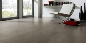 Modernes Wohnzimmer mit großen Fenstern, grauem Laminatboden, einem weißen Stuhl, roten Kissen und dekorativen Vasen auf einem weißen Regal. Durch die Fenster ist das Stadtbild zu sehen. -Bodenstyle Schuster - Industriestraße 2 - 66802 Überherrn - +49 (0)6836-7789955