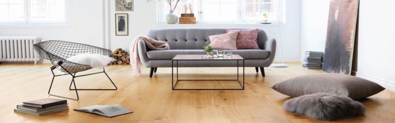 Ein modernes Wohnzimmer mit grauem Sofa, Drahtsessel, Couchtisch, großem Kissen, Büchern und minimalistischem Dekor auf stilvollem Parkettboden. -Bodenstyle Schuster - Industriestraße 2 - 66802 Überherrn - +49 (0)6836-7789955
