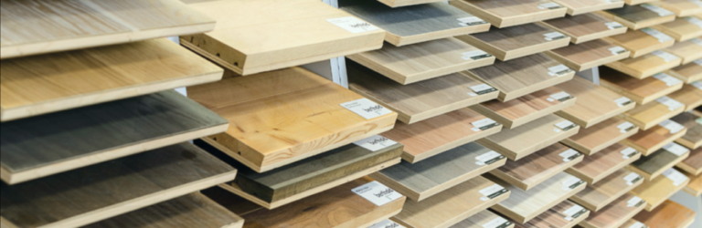 Ausstellungsregale mit verschiedenen Holzbodenmustern in unterschiedlichen Oberflächen und Farbtönen, einschließlich Laminat- und Vinylbelag-Optionen, jedes Muster zur Identifizierung beschriftet. -Bodenstyle Schuster - Industriestraße 2 - 66802 Überherrn - +49 (0)6836-7789955