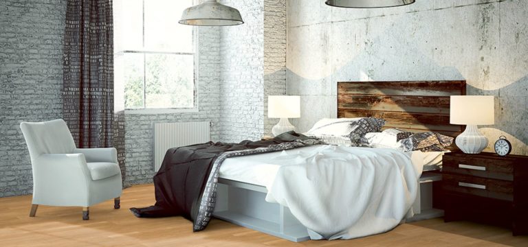 Modernes Schlafzimmer mit einem großen Bett, einem Kopfteil aus Holz, Beistelltischen mit Lampen, einem Sessel und sichtbaren Backsteinwänden. Laminat-Bodenbeläge sorgen für Wärme und Stil, alles schön beleuchtet von natürlichem Licht aus einem Fenster. -Bodenstyle Schuster - Industriestraße 2 - 66802 Überherrn - +49 (0)6836-7789955