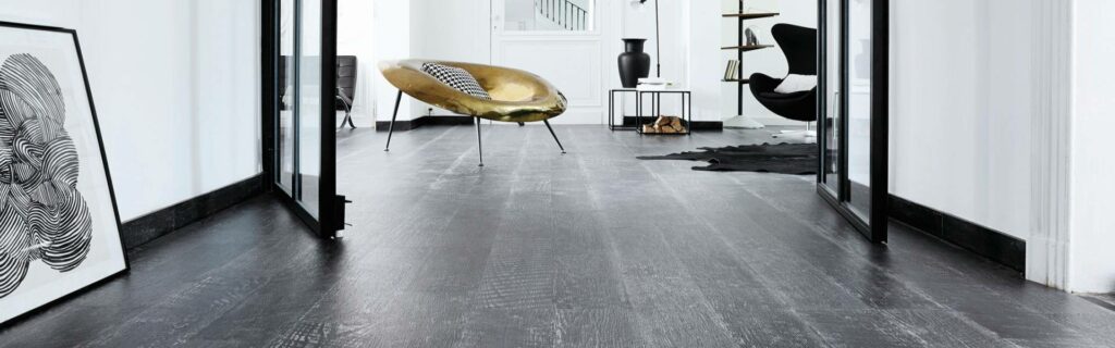 Modernes, minimalistisches Interieur mit Parkettboden aus dunklem Holz, Glastüren, einem goldenen Sessel, abstrakten Kunstwerken und schwarz-weißen Dekorelementen für eine raffinierte Bodenbeläge-Ästhetik. -Bodenstyle Schuster - Industriestraße 2 - 66802 Überherrn - +49 (0)6836-7789955