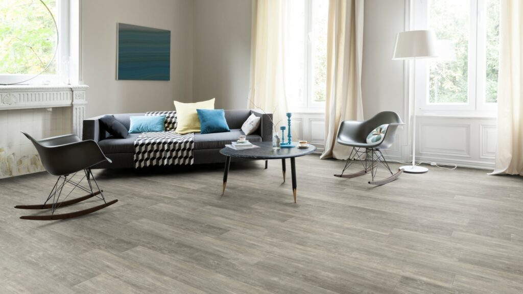 Modernes Wohnzimmer mit grauem Sofa, zwei schwarzen Stühlen, rundem Couchtisch, Stehlampe, Wandkunst und großen Fenstern mit hellen Vorhängen. Der helle Holzfußboden eines erfahrenen Bodenlegers unterstreicht das neutrale Farbschema. -Bodenstyle Schuster - Industriestraße 2 - 66802 Überherrn - +49 (0)6836-7789955
